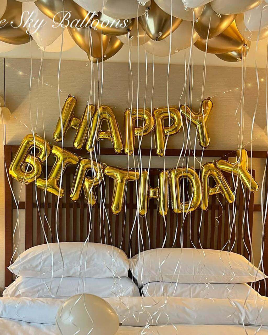 Gold 'Happy Birthday' balloons above a bed in a bedroom setting.