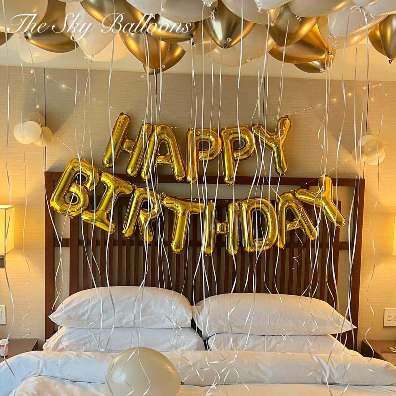 Gold 'Happy Birthday' balloons above a bed in a bedroom setting.