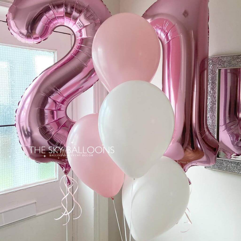 Pink and white balloons shaped like the number '21' in a room setting.