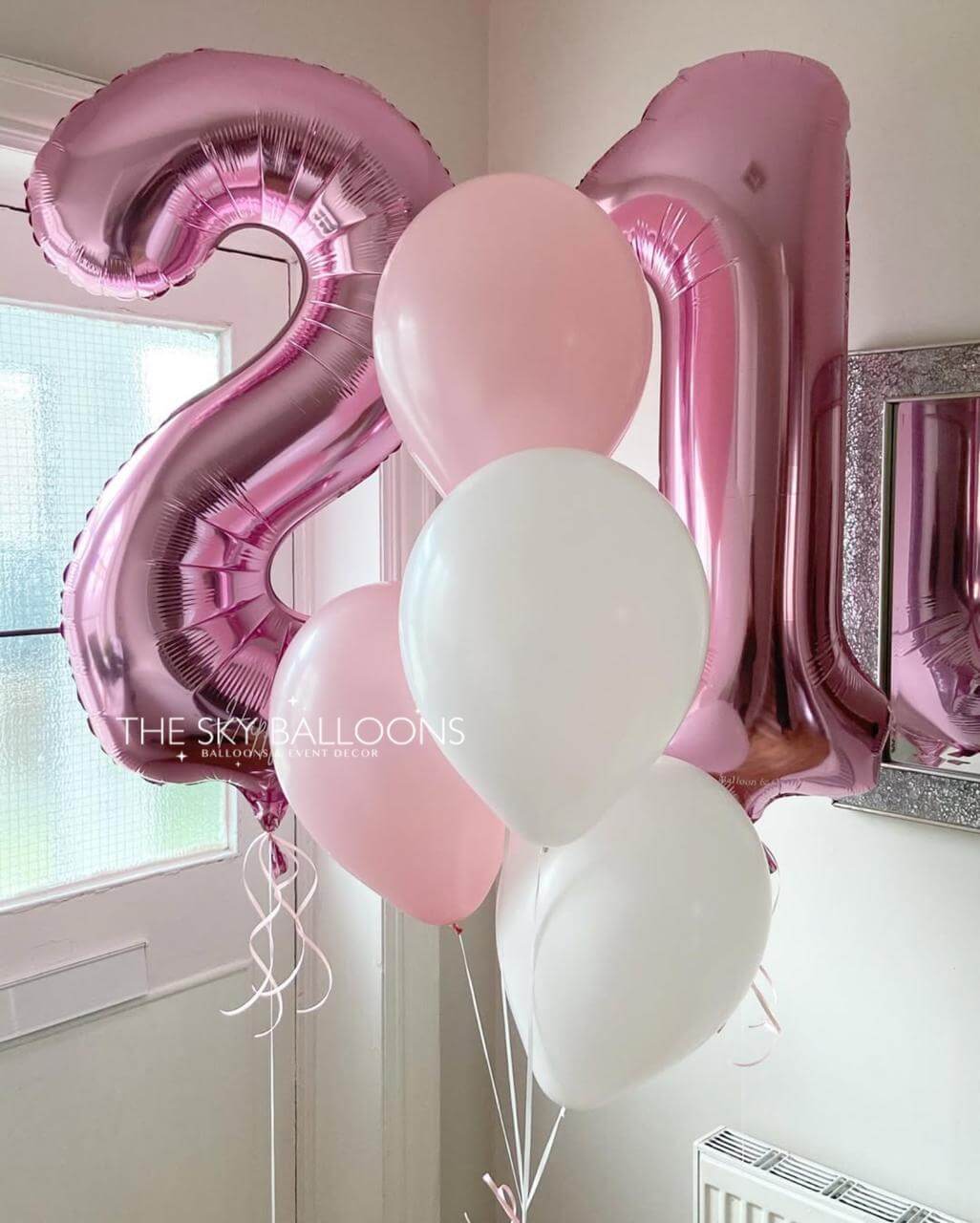 Pink and white balloons shaped like the number '21' in a room setting.