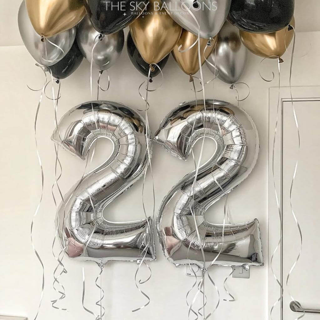 Silver number '22' balloons with gold, black, and silver balloons against a white wall.