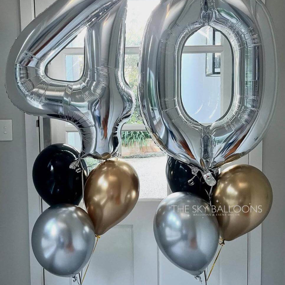 Silver number '40' balloons with smaller gold, black, and silver balloons against a white door background.