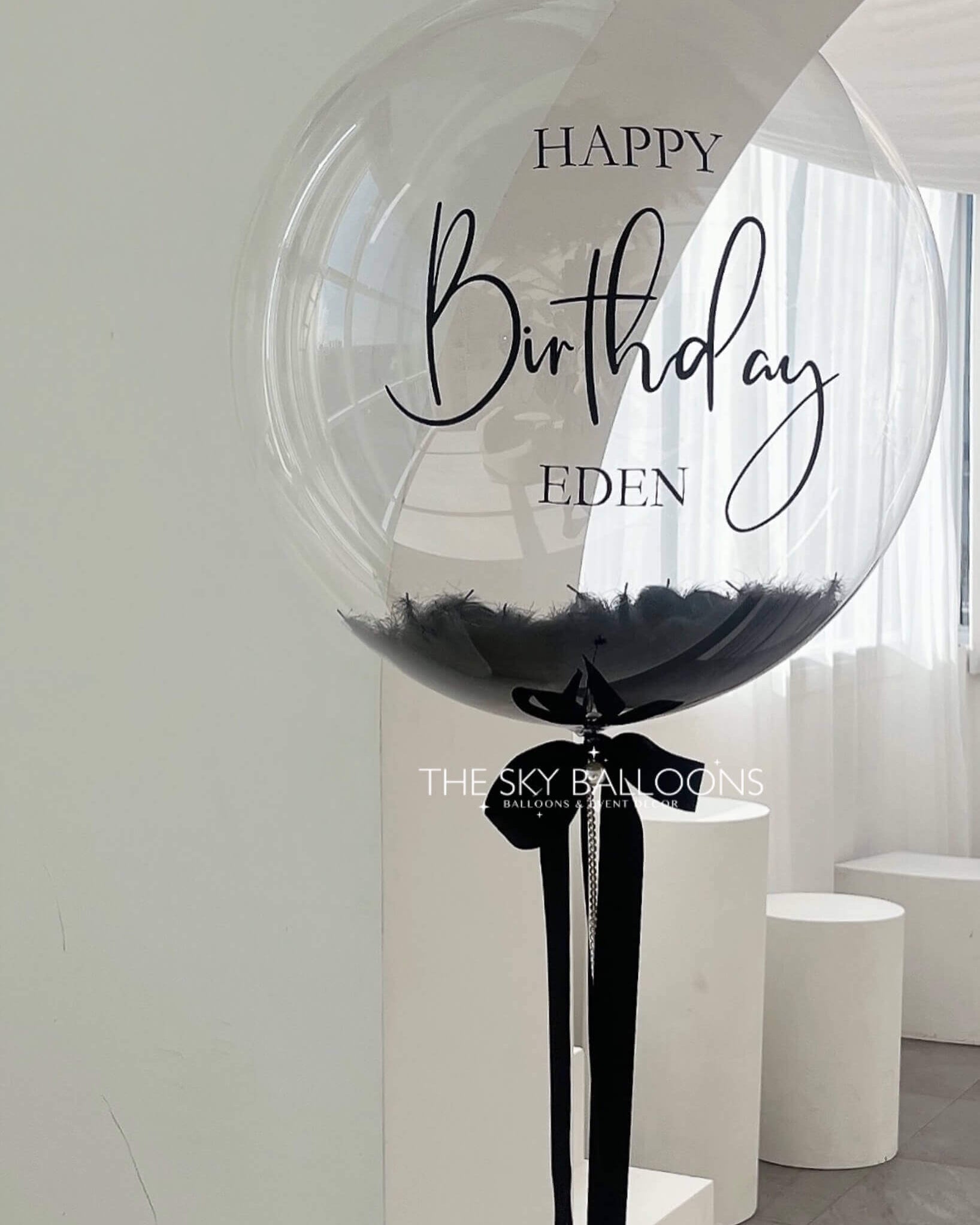 Large transparent balloon with 'Happy Birthday Eden' text in a modern indoor setting.