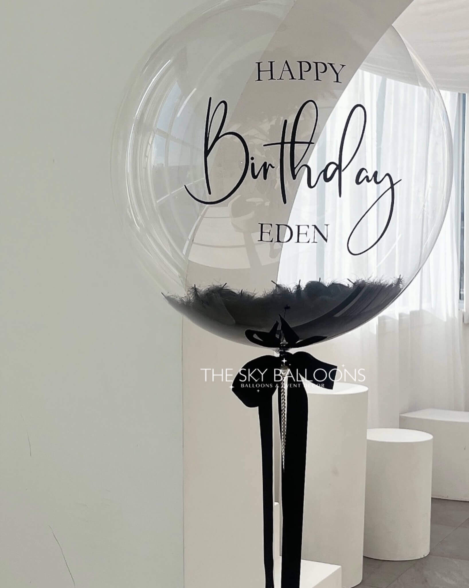 Large transparent balloon with 'Happy Birthday Eden' text in a modern indoor setting.