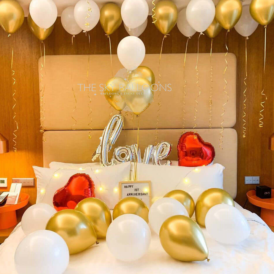 Bed decorated with gold and white balloons, including a heart-shaped balloon.