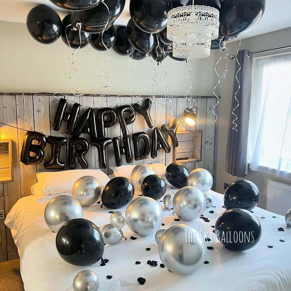 Monochrome Happy Birthday balloon display with black, white and silver balloons plus star-shaped balloons in bedroom setting