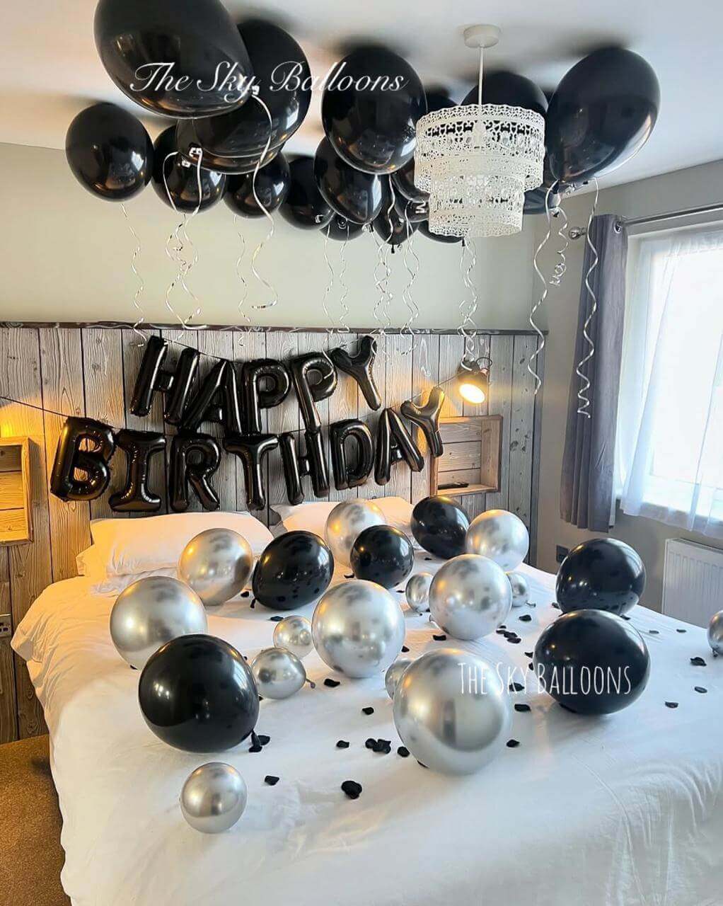 Monochrome Happy Birthday balloon display with black, white and silver balloons plus star-shaped balloons in bedroom setting