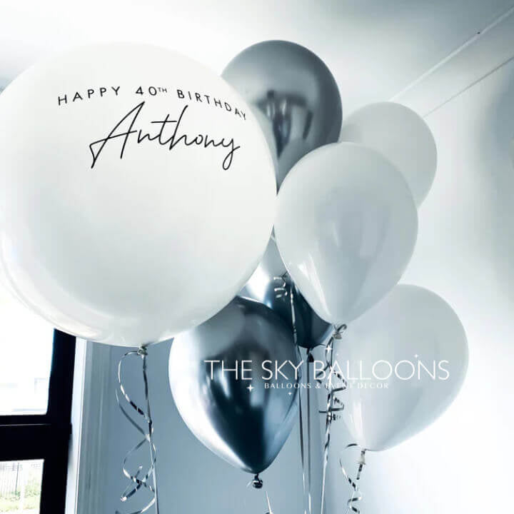 A set of balloons including white and black balloons with one personalized balloon that reads 'Happy 40th Birthday Anthony'.