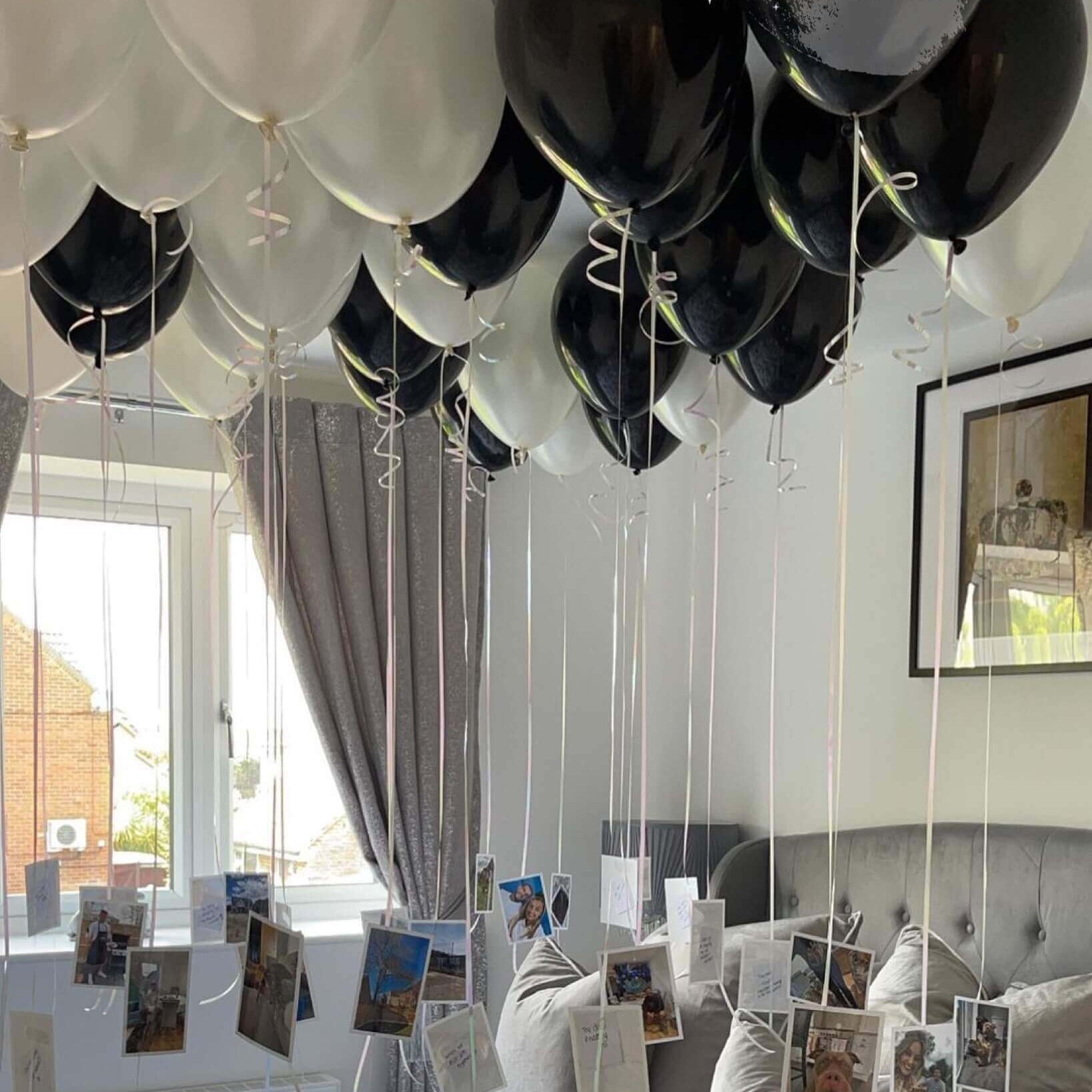 A room setup with black and white balloons arranged for an event, with printed photographs attached to the balloons.