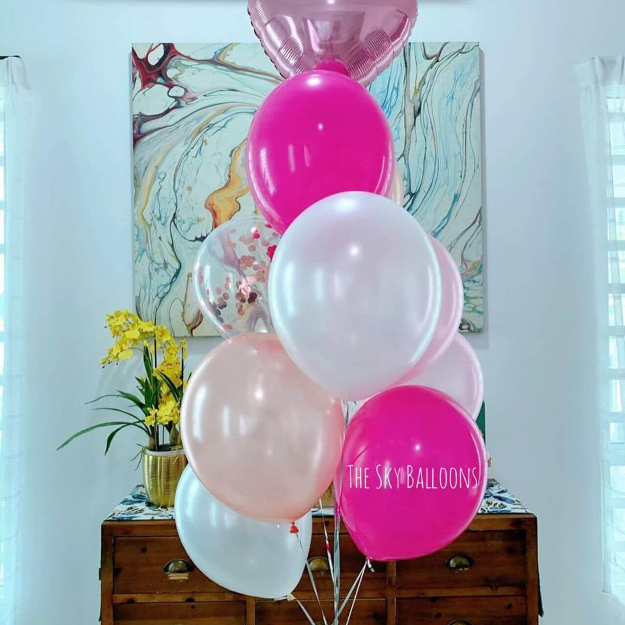 Pink, white, and heart-shaped balloons with 'The Sky Balloons' logo on a wooden cabinet.