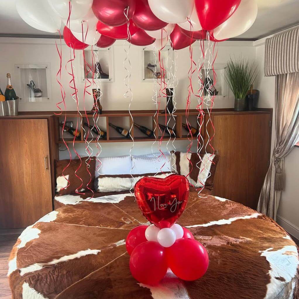 Red and white balloons with a heart-shaped balloon on a cowhide rug in a room.