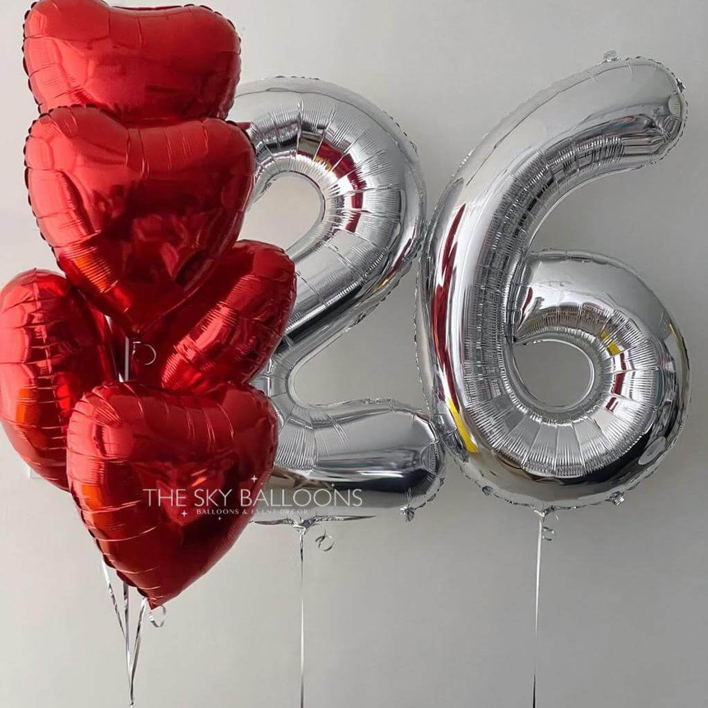 Red heart-shaped balloons and silver number '26' balloon against a white background