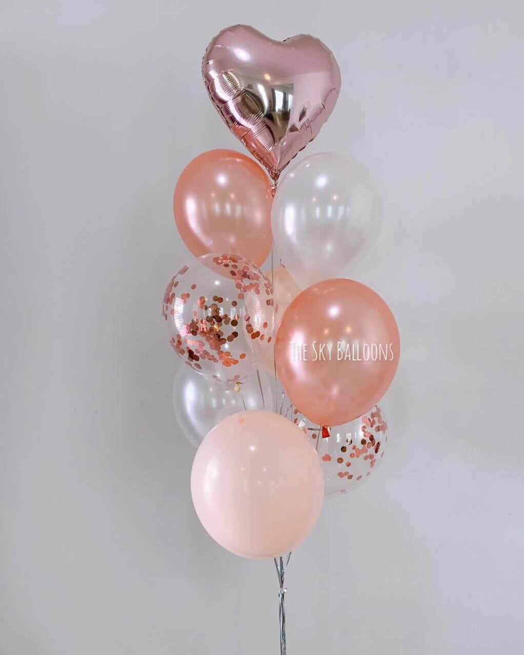 Bouquet of balloons with pink, clear, and heart-shaped balloons on a light gray background.