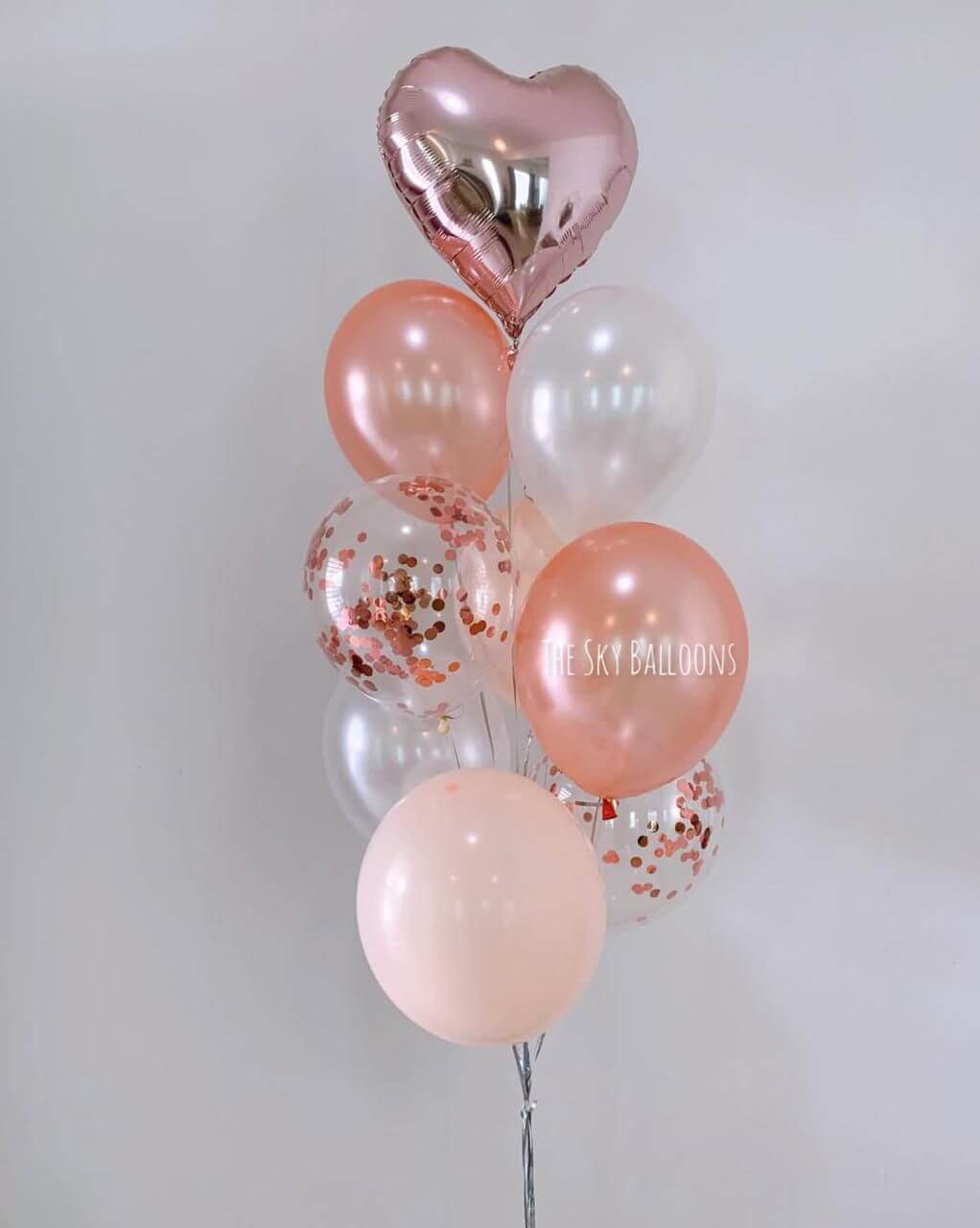 Bouquet of balloons with pink, clear, and heart-shaped balloons on a light gray background.