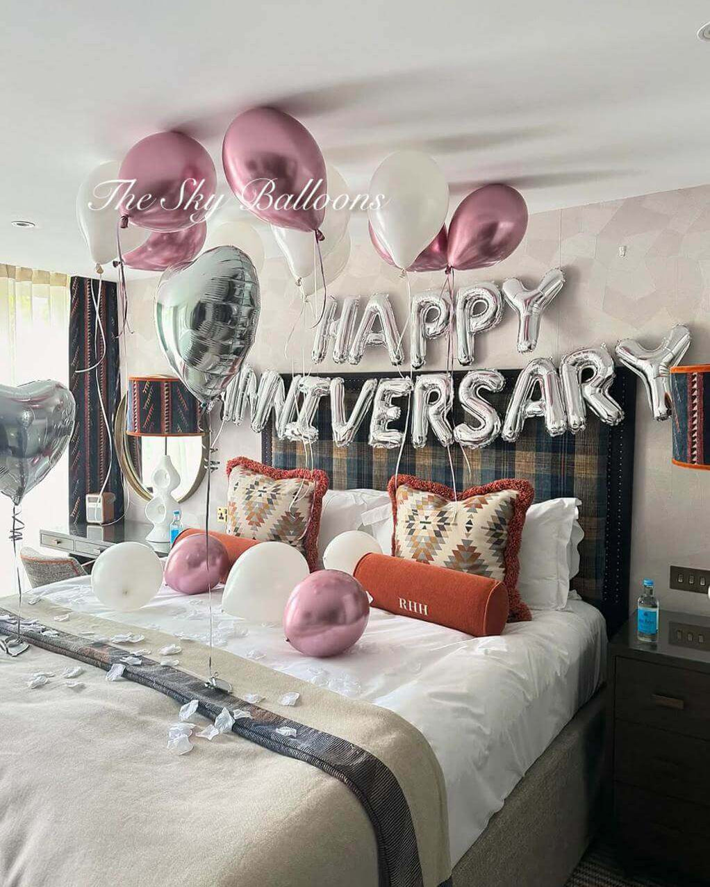 Decorated bedroom with 'Happy Anniversary' balloons and pillows.