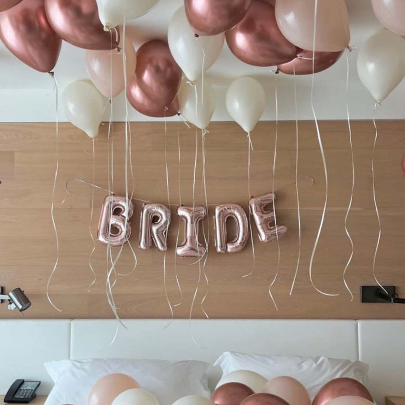 Rose gold and white balloons with 'BRIDE' letter balloons on a wooden surface.