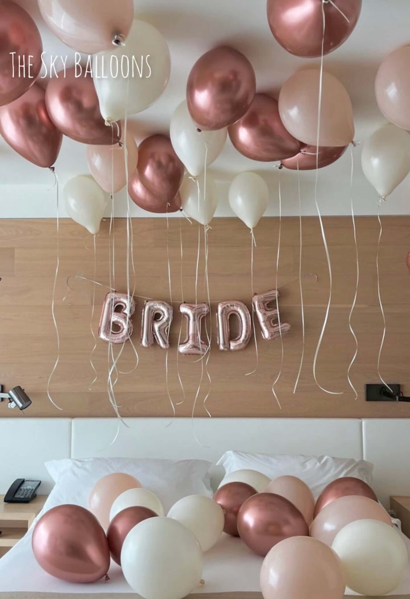 Rose gold and white balloons with 'BRIDE' letter balloons on a wooden surface.
