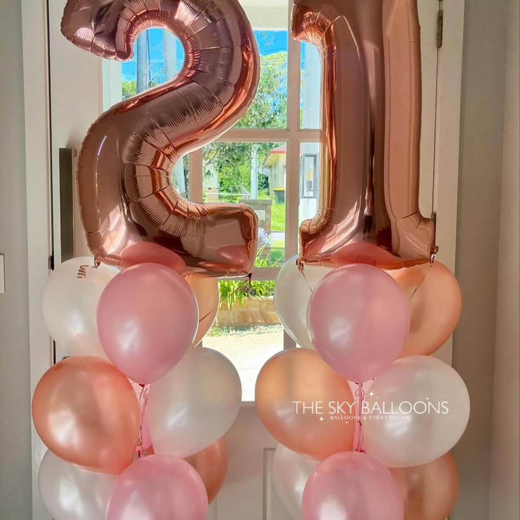 Rose gold number '21' balloons with pink and white balloons against a door background.