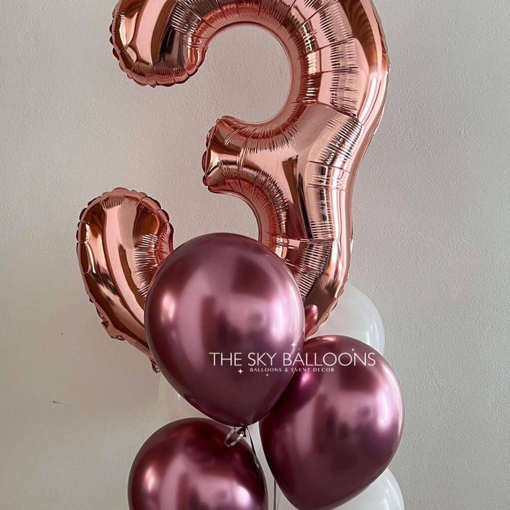 Rose gold number '3' balloon with pink balloons on a light gray background