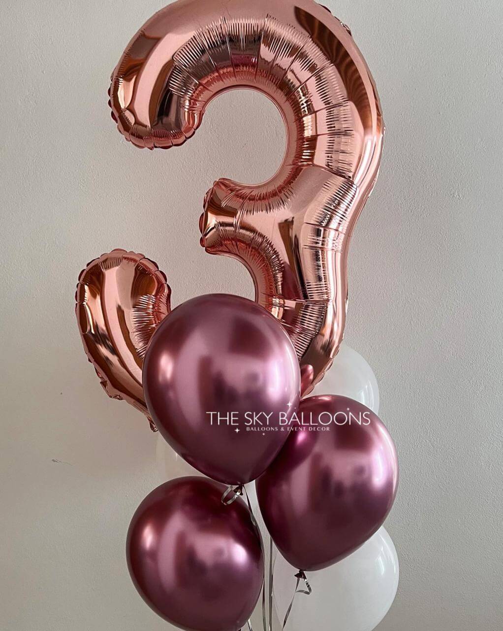 Rose gold number '3' balloon with pink balloons on a light gray background