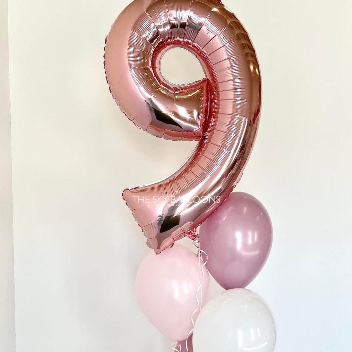 Rose gold number 9 balloon with smaller pink and white balloons on a light background