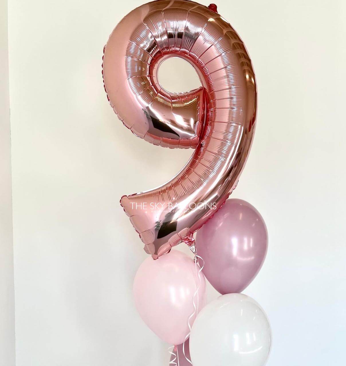 Rose gold number 9 balloon with smaller pink and white balloons on a light background