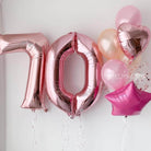 Rose gold number balloons spelling '70' on a white background with additional pink balloons.