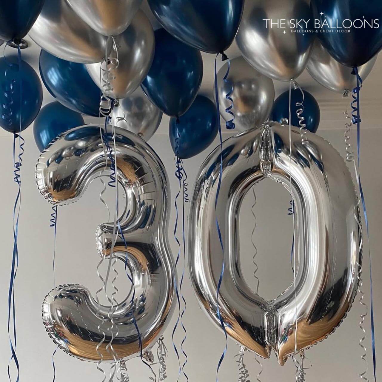 Silver '30' balloons with blue and silver ribbons against a neutral background
