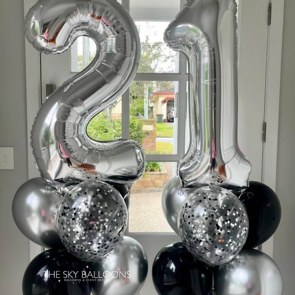 Silver and black balloons shaped like the number '21' in front of a door.