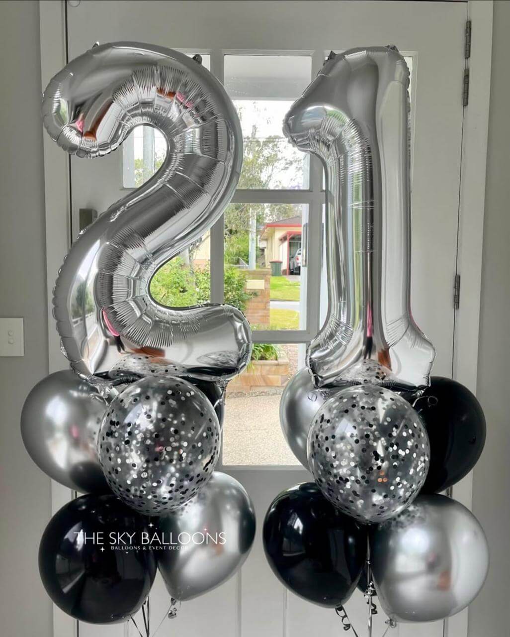 Silver and black balloons shaped like the number '21' in front of a door.