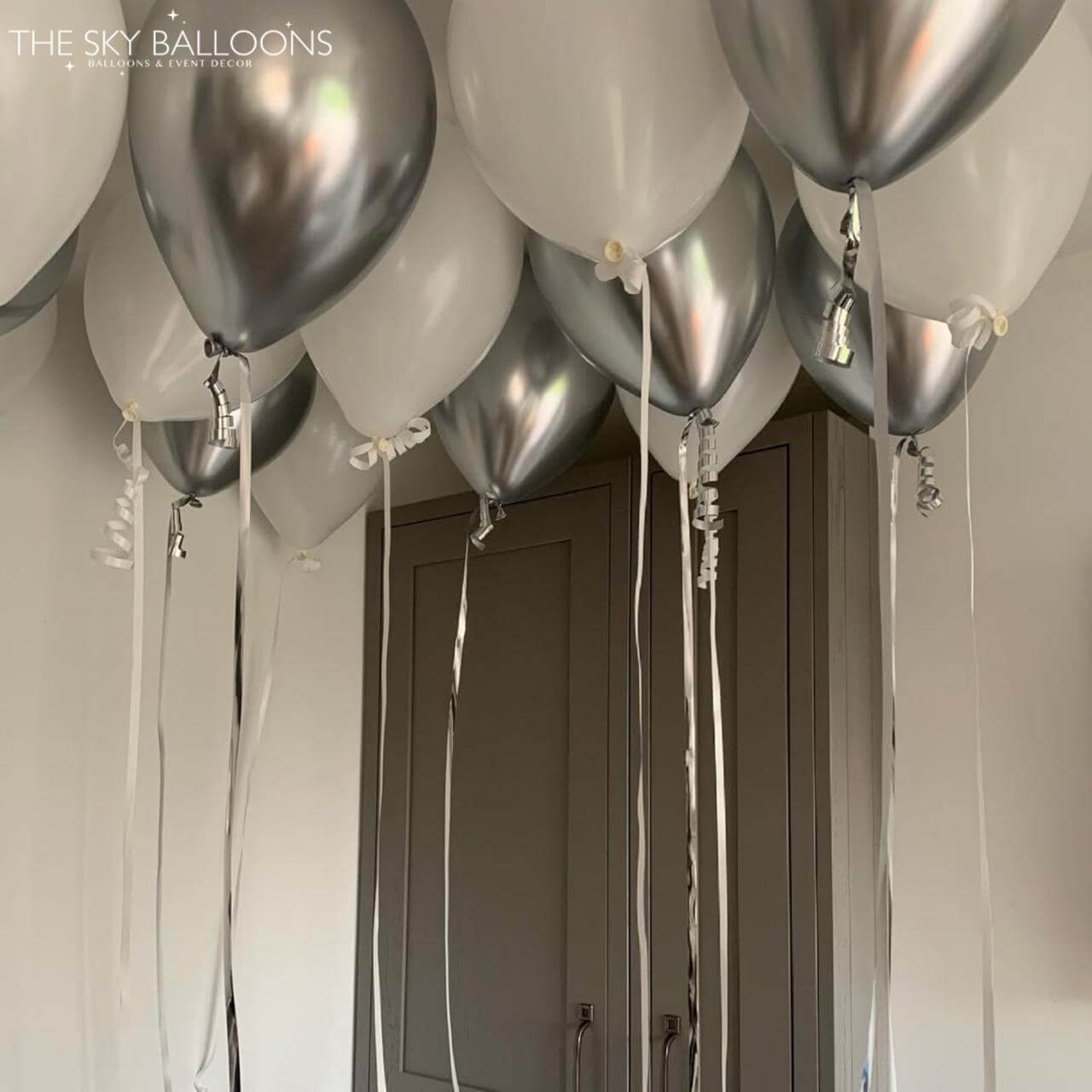 Silver and white balloons with ribbons hanging in a room.