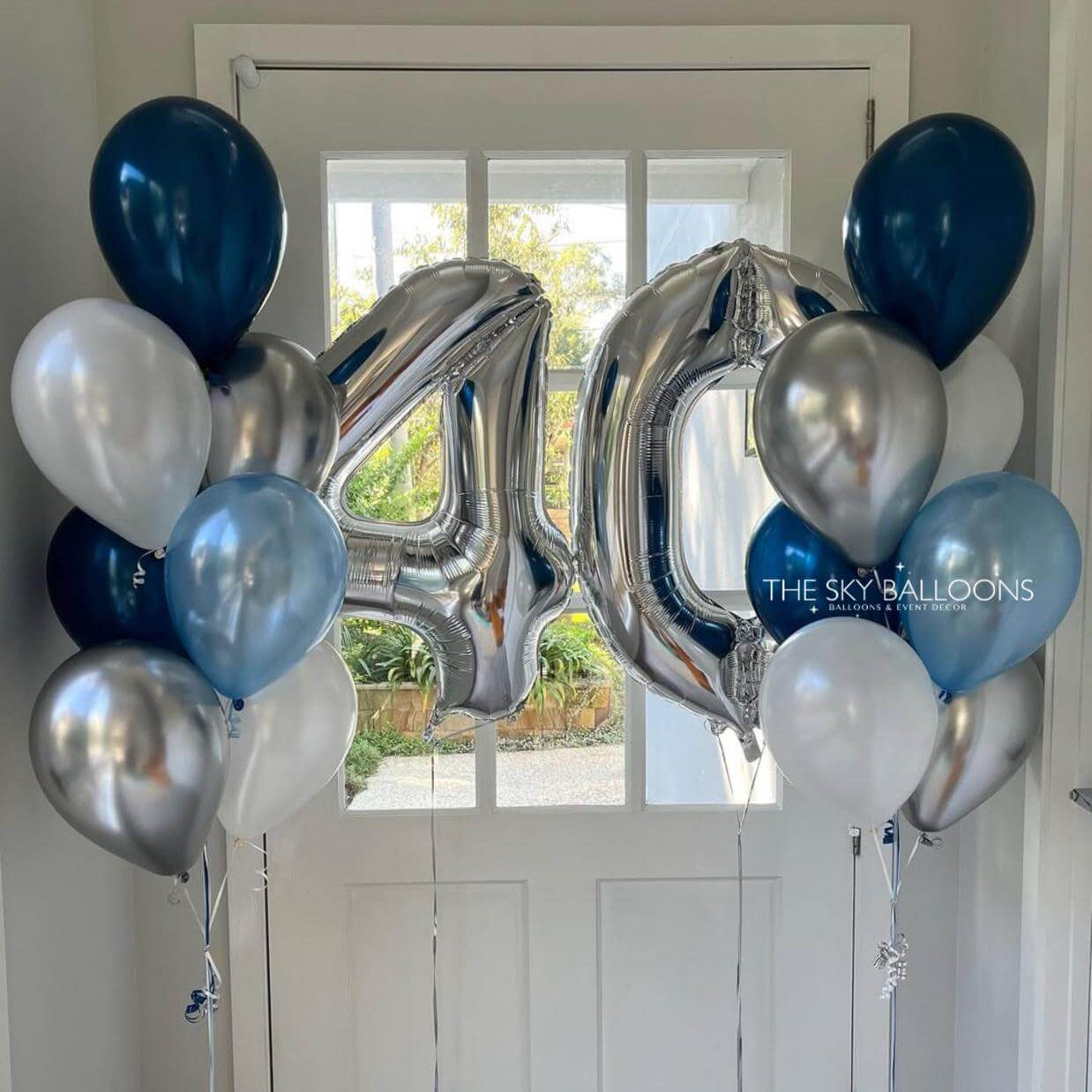 Silver, blue, and white balloons arranged to spell out '40' in front of a door.