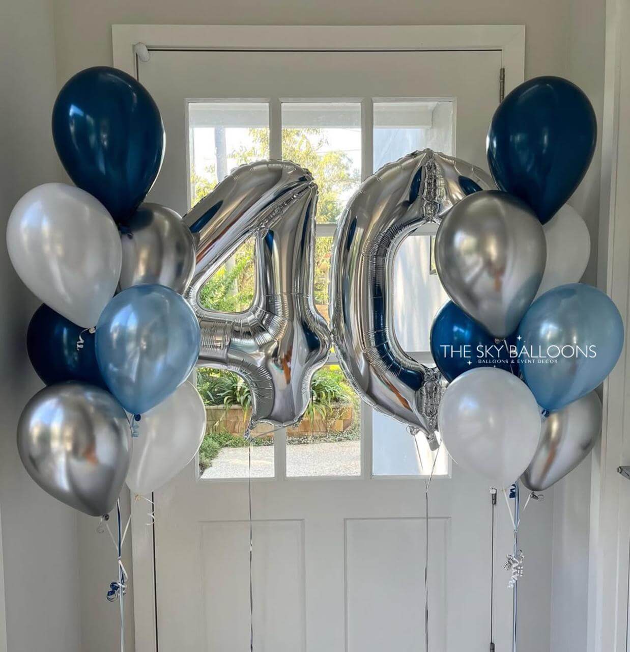Silver, blue, and white balloons arranged to spell out '40' in front of a door.