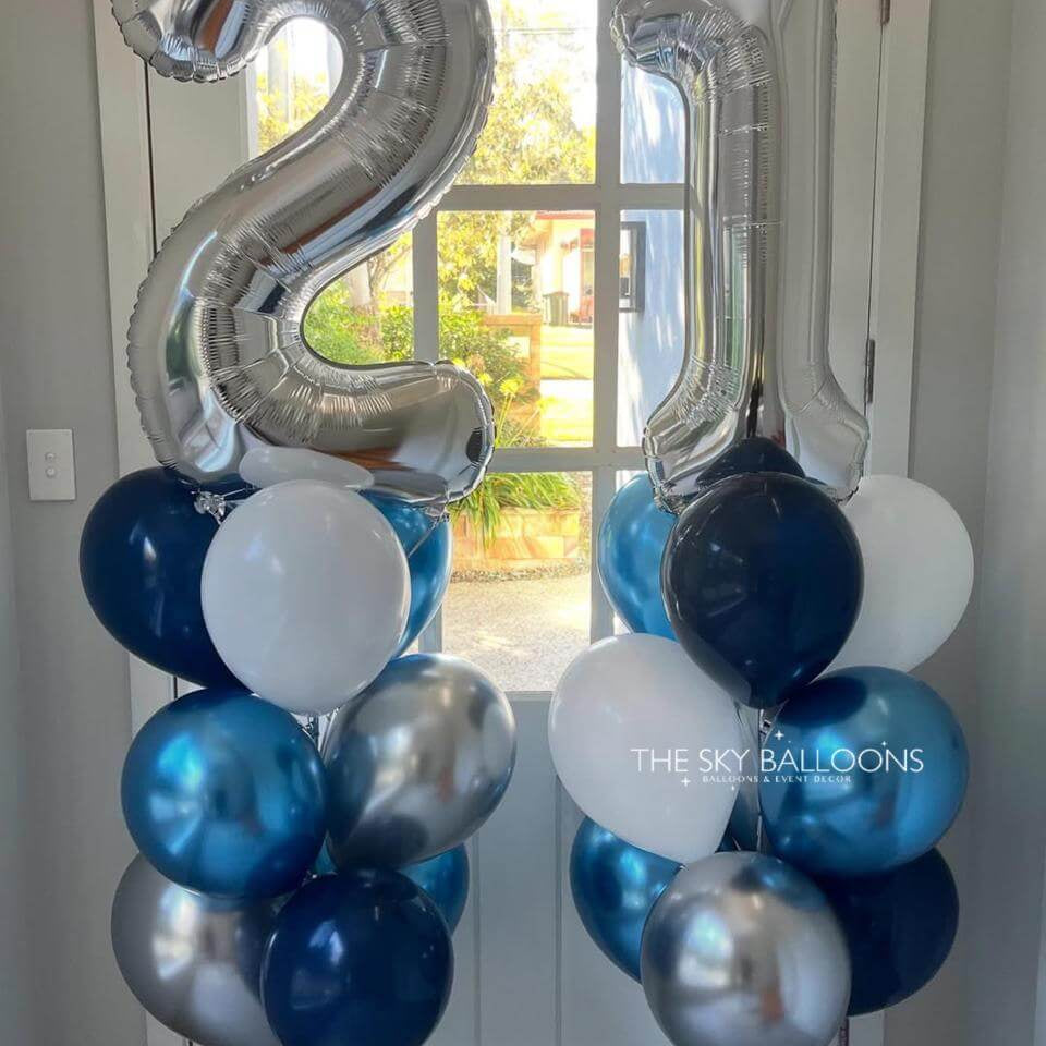Silver, blue, and white balloons shaped like the number '21' in a room with a window.