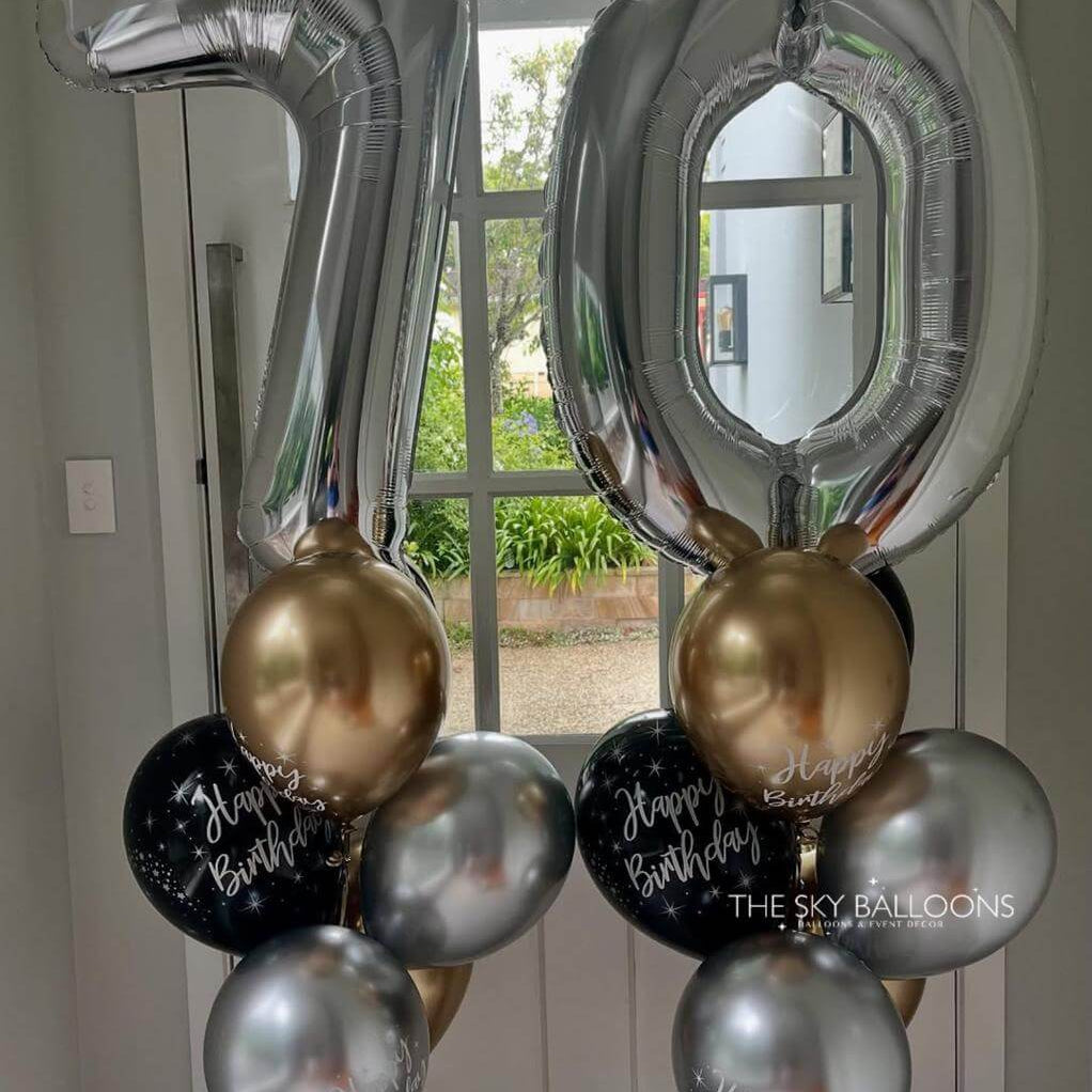 Silver, gold, and black balloons with '70' and 'Happy Birthday' text against a neutral background.