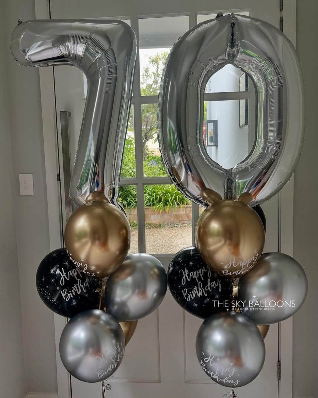 Silver, gold, and black balloons with '70' and 'Happy Birthday' text against a neutral background.