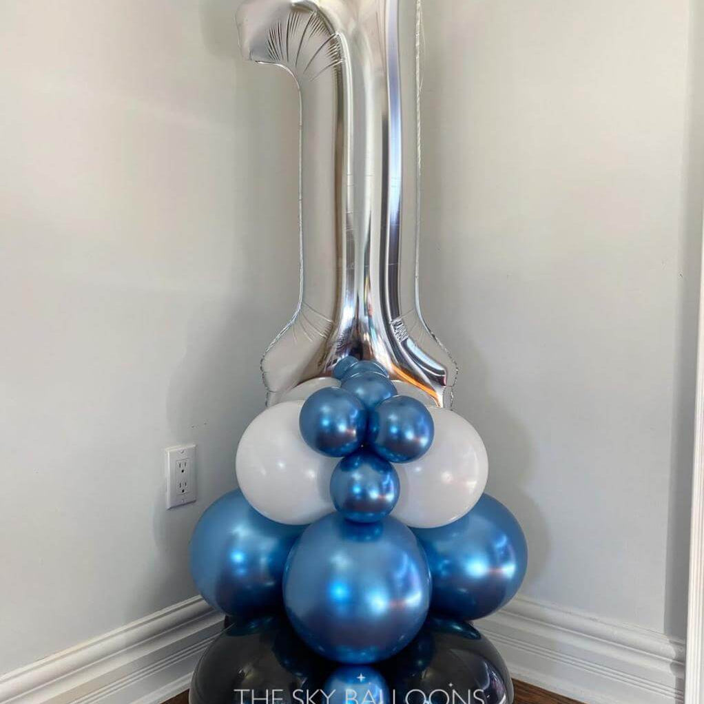 Silver number '1' balloon with blue and white balloons against a plain wall.