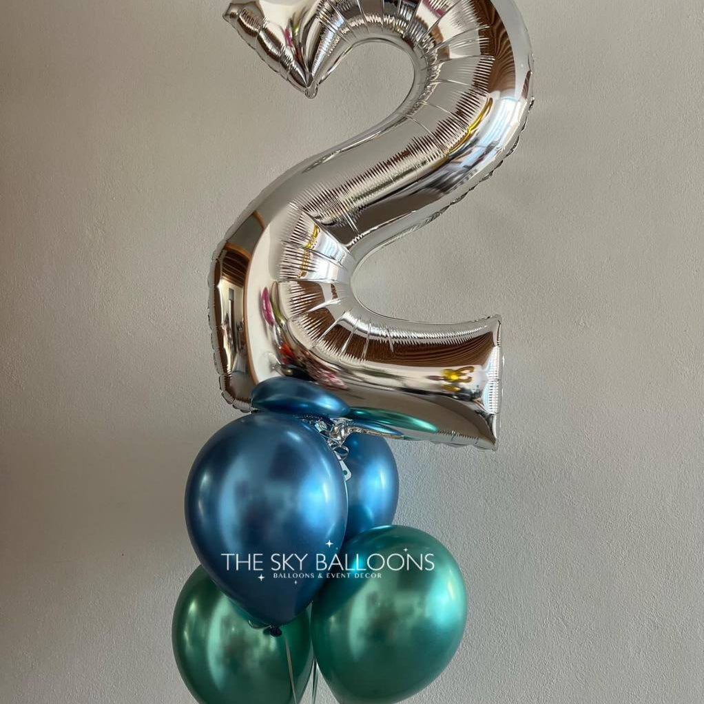 Silver number '2' balloon with blue and green balloons against a plain background