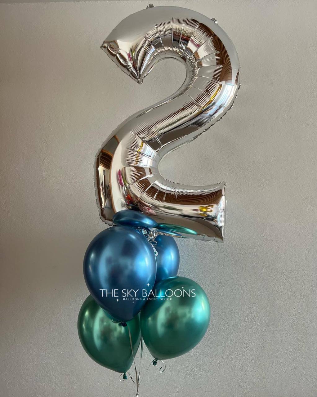 Silver number '2' balloon with blue and green balloons against a plain background