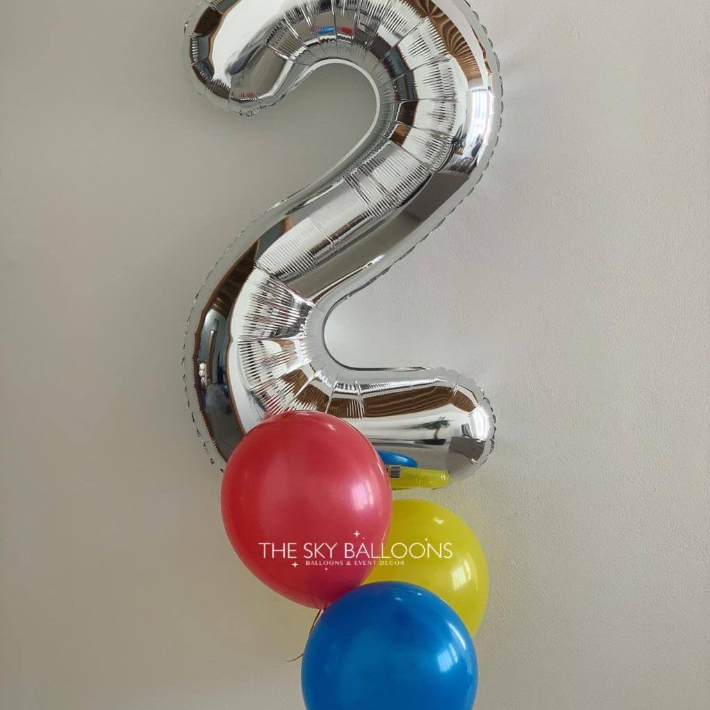 Silver number 2 balloon with red, blue, and yellow balloons on a plain background