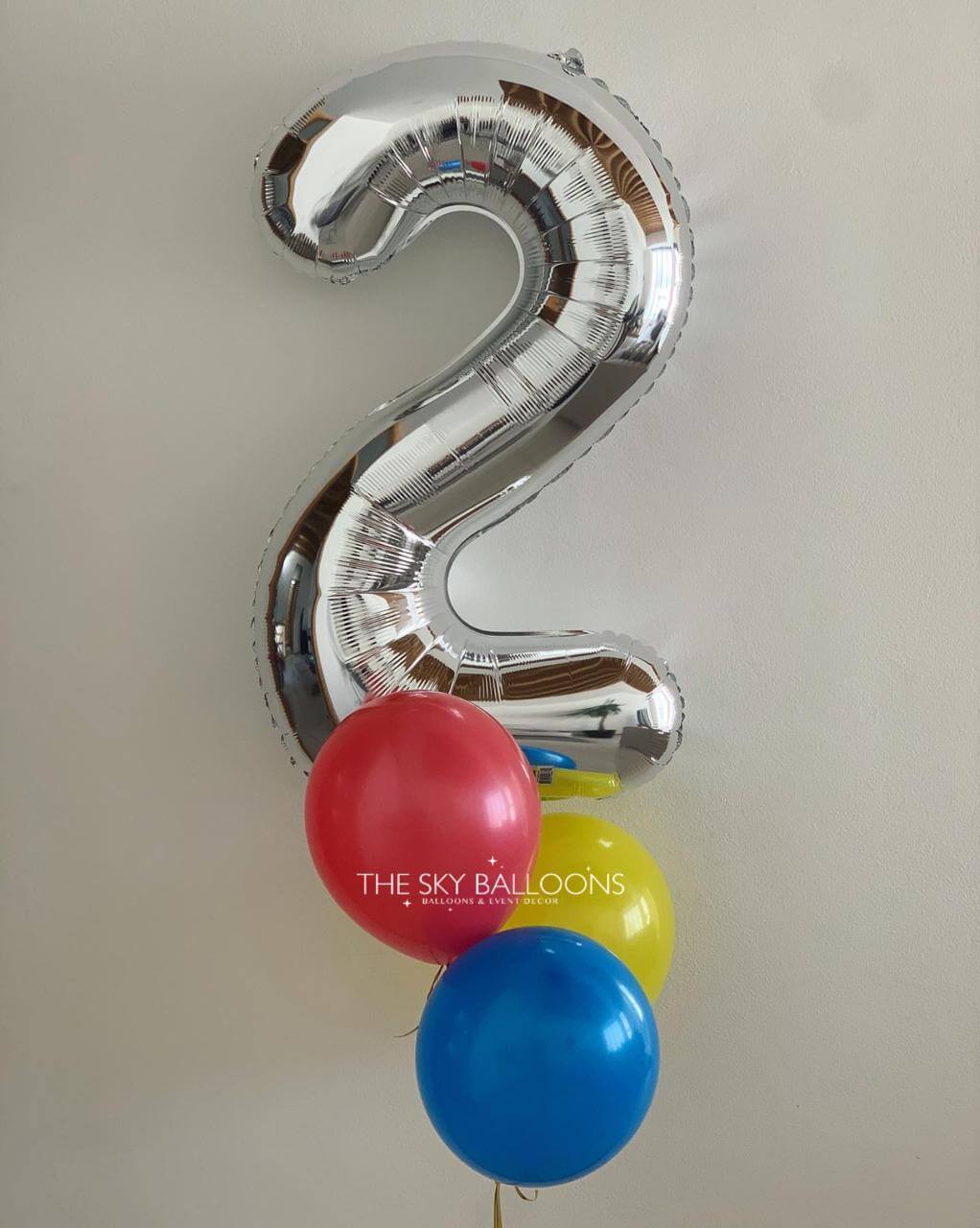 Silver number 2 balloon with red, blue, and yellow balloons on a plain background
