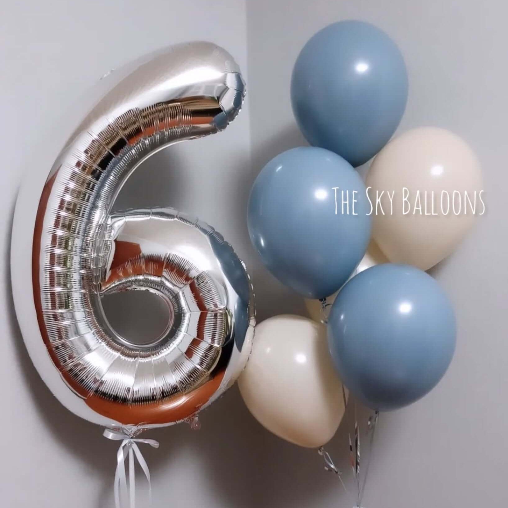 Silver number 6 balloon and blue and white balloons against a light gray background.