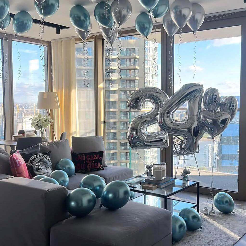 Decorative balloons, including large silver '24', in a living room with cityscape view.