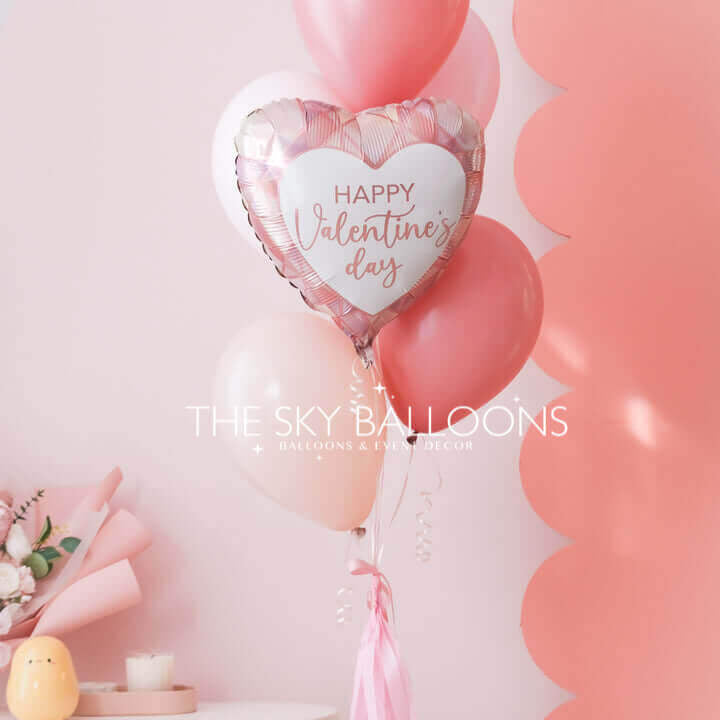Valentine's Day balloon bouquet with a pink heart-shaped foil balloon reading "Happy Valentine's Day" and pink and blush latex balloons, tied with a pink tassel ribbon.