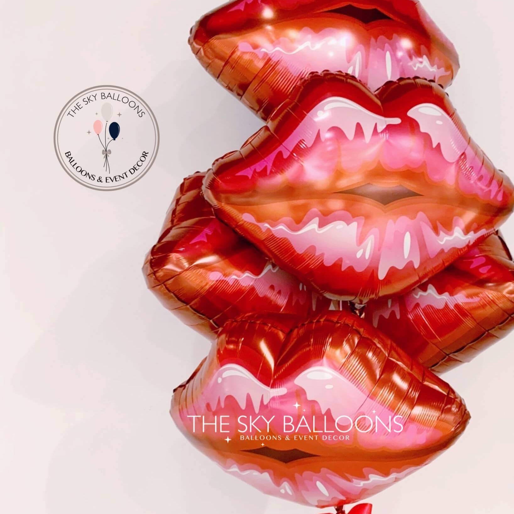 A set of inflated red and pink colored balloons in the shape of lips, with a label at the top left corner reading 'The Sky Balloons'.