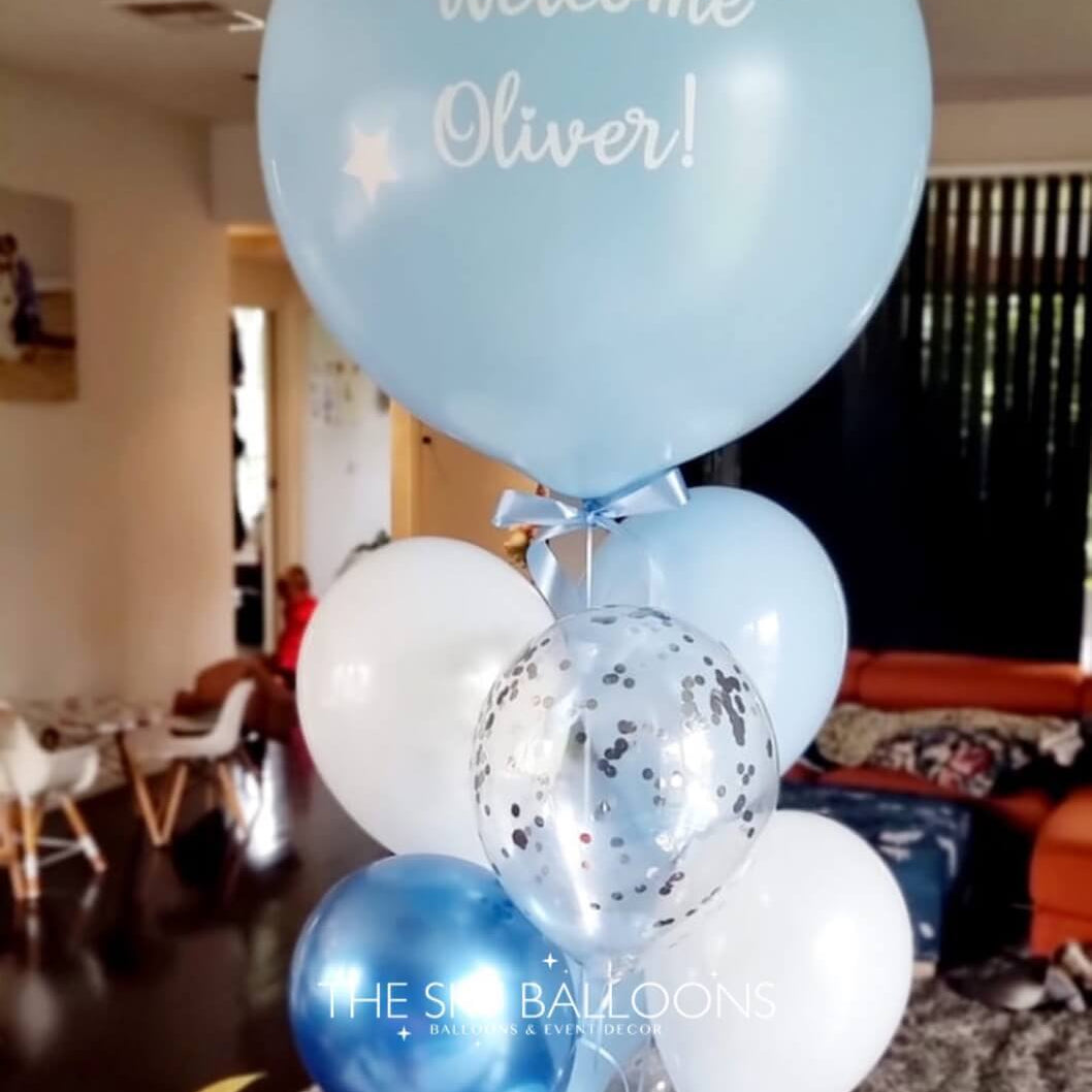 Decorative balloon arrangement with 'Welcome Oliver!' text in a room setting.