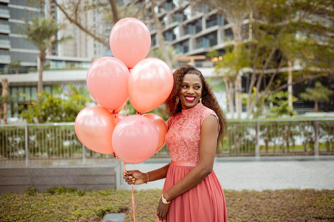Woman in a pink dress holding pink balloons outdoors.