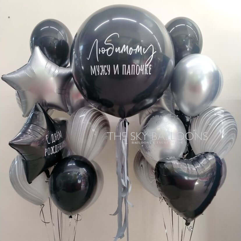 A bouquet of balloons including a mix of latex and foil balloons in black, silver, and white colors, with star and heart shapes, displayed against a plain background.