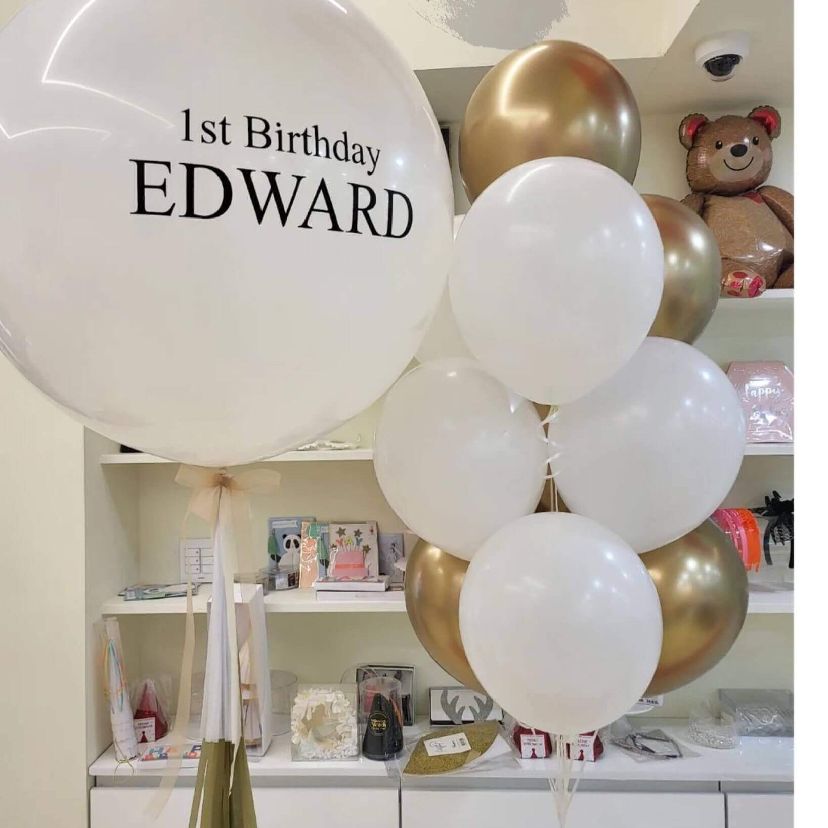 A balloon bouquet featuring a customized '1st Birthday' balloon with the name 'Edward' printed on it, along with several other latex balloons in varying sizes.