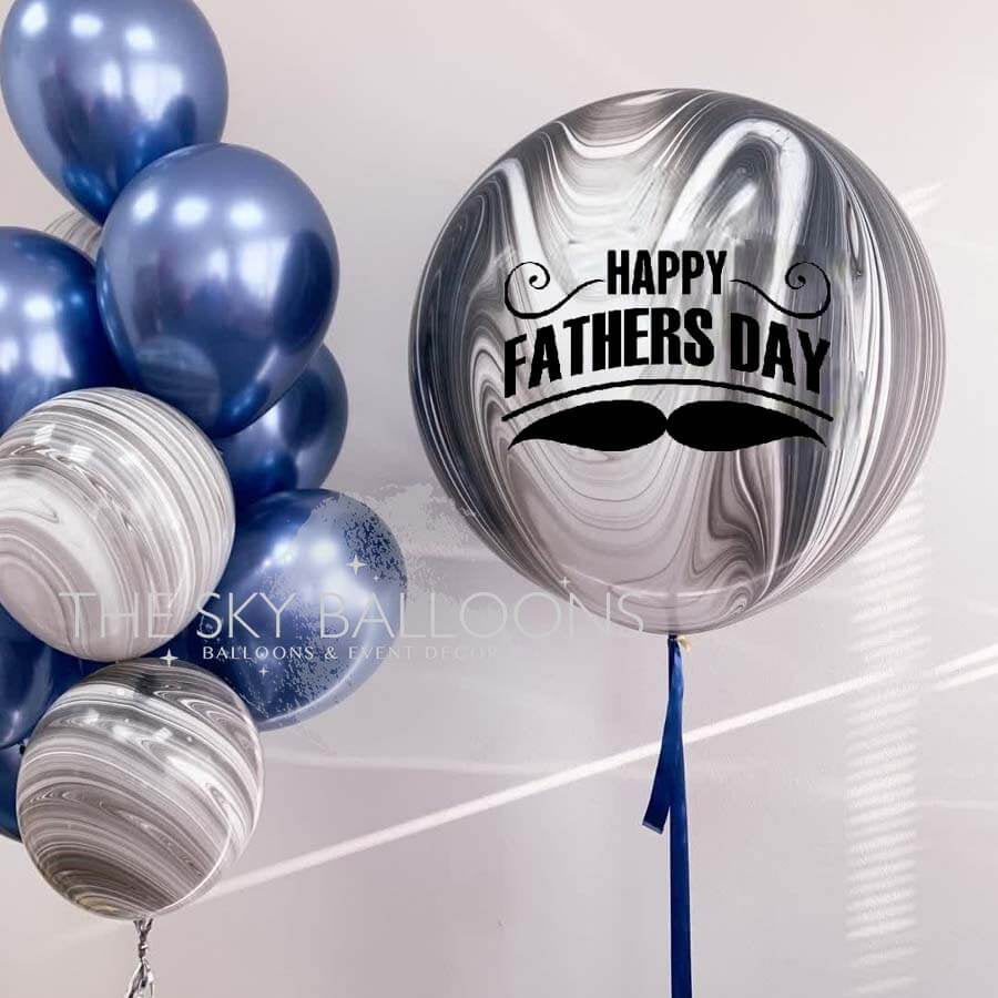 A bouquet of round, silver-colored balloons with the text 'Happy Father's Day' printed on one of them, alongside a large customized balloon with a 'Happy Father's Day' message and a graphic of a mustache.